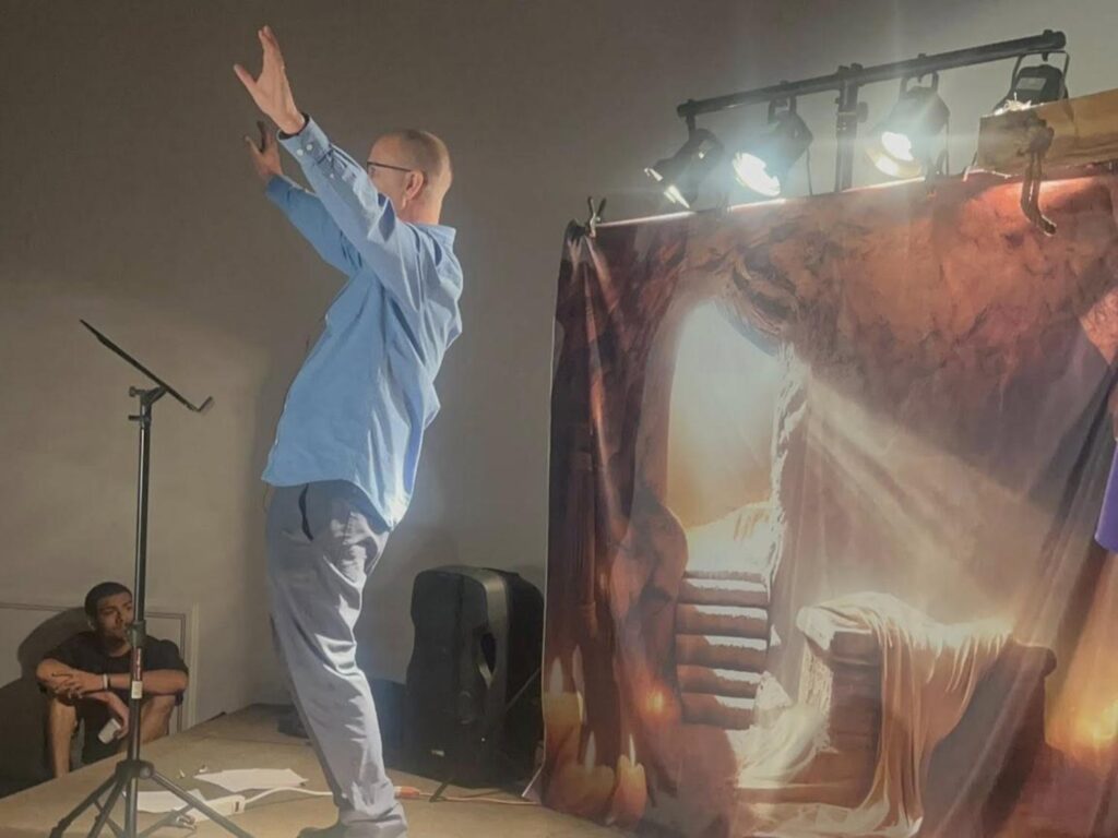 Pastor Peter Schalembier preaching in front of tapestry of empty tomb from Porterville First Assembly of God Easter service